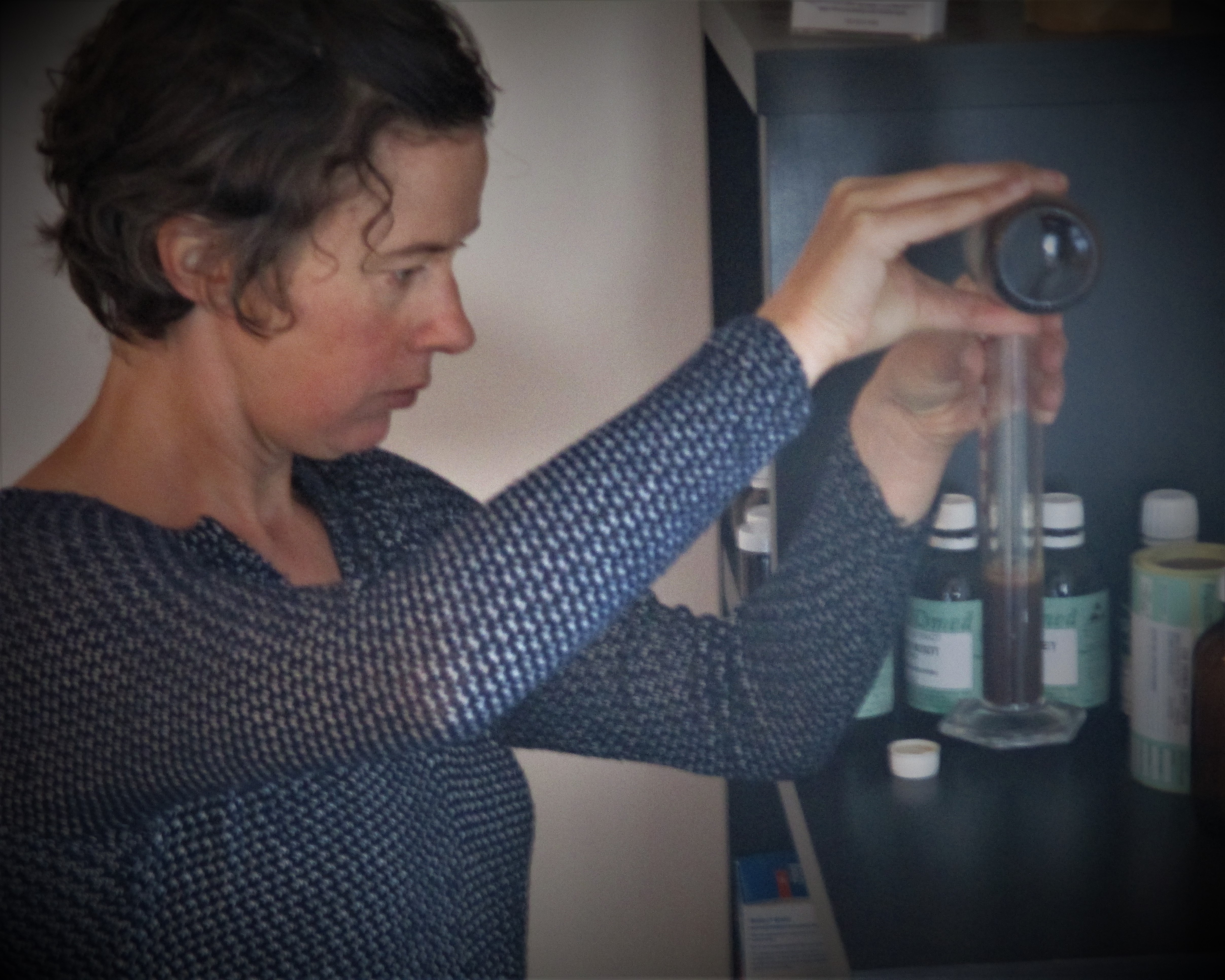A person carefully pouring a liquid into a graduated cylinder in a laboratory setting.