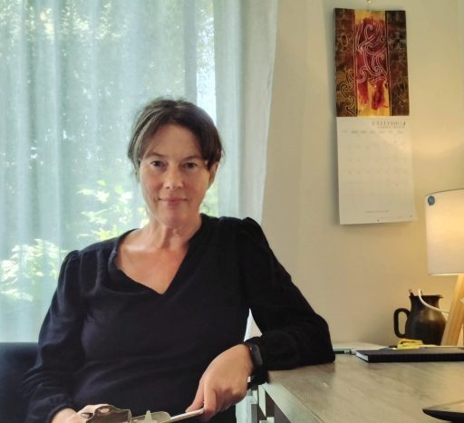 A women sitting on a chair at a desk, holding a clipboard, with her elbow on the table